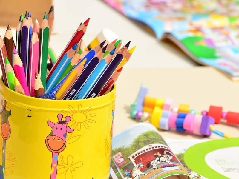 Abbildung von Buntstiften in einer gelben Dose mit Kindermotiven