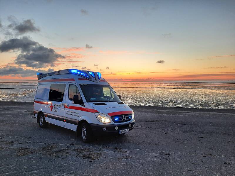 Foto eines Wagens vom Roten Kreuz mit Blaulicht am Strand im Sonnenuntergang